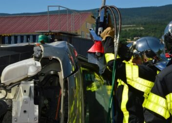 Firefighters in helmets and uniforms conducting an extrication on an overturned vehicle outdoors.