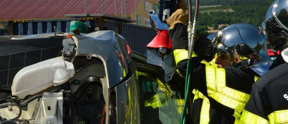 Firefighters in helmets and uniforms conducting an extrication on an overturned vehicle outdoors.