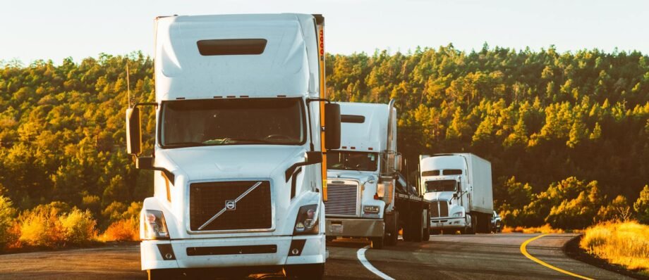 Three semi trucks driving on a highway through a forested landscape in Arizona.