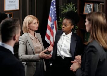 Diverse group of professionals in a discussion in a formal setting with an American flag.