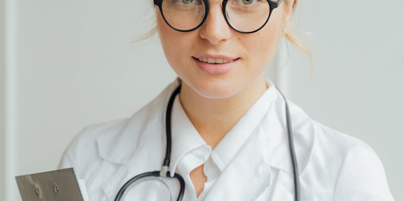 Smiling female healthcare professional in white coat holding clipboard indoors.