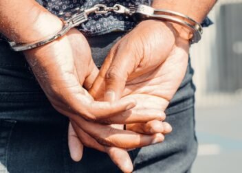Rear view of a person in handcuffs outdoors, symbolizing law enforcement and justice.