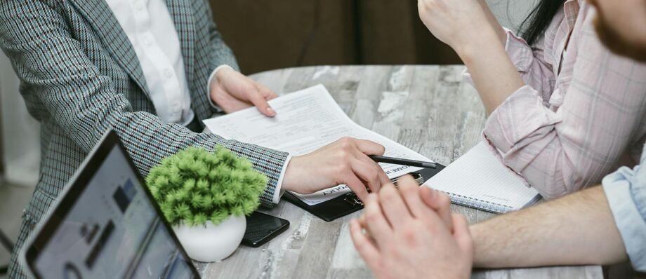 Professional meeting discussing business agreements with laptops and documents on a rustic table.