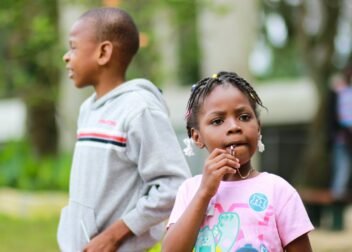 selective focus photography of girl biting her pendant beside a boy in gray pullover hoodie