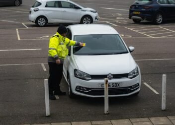 man in yellow jacket standing beside white car