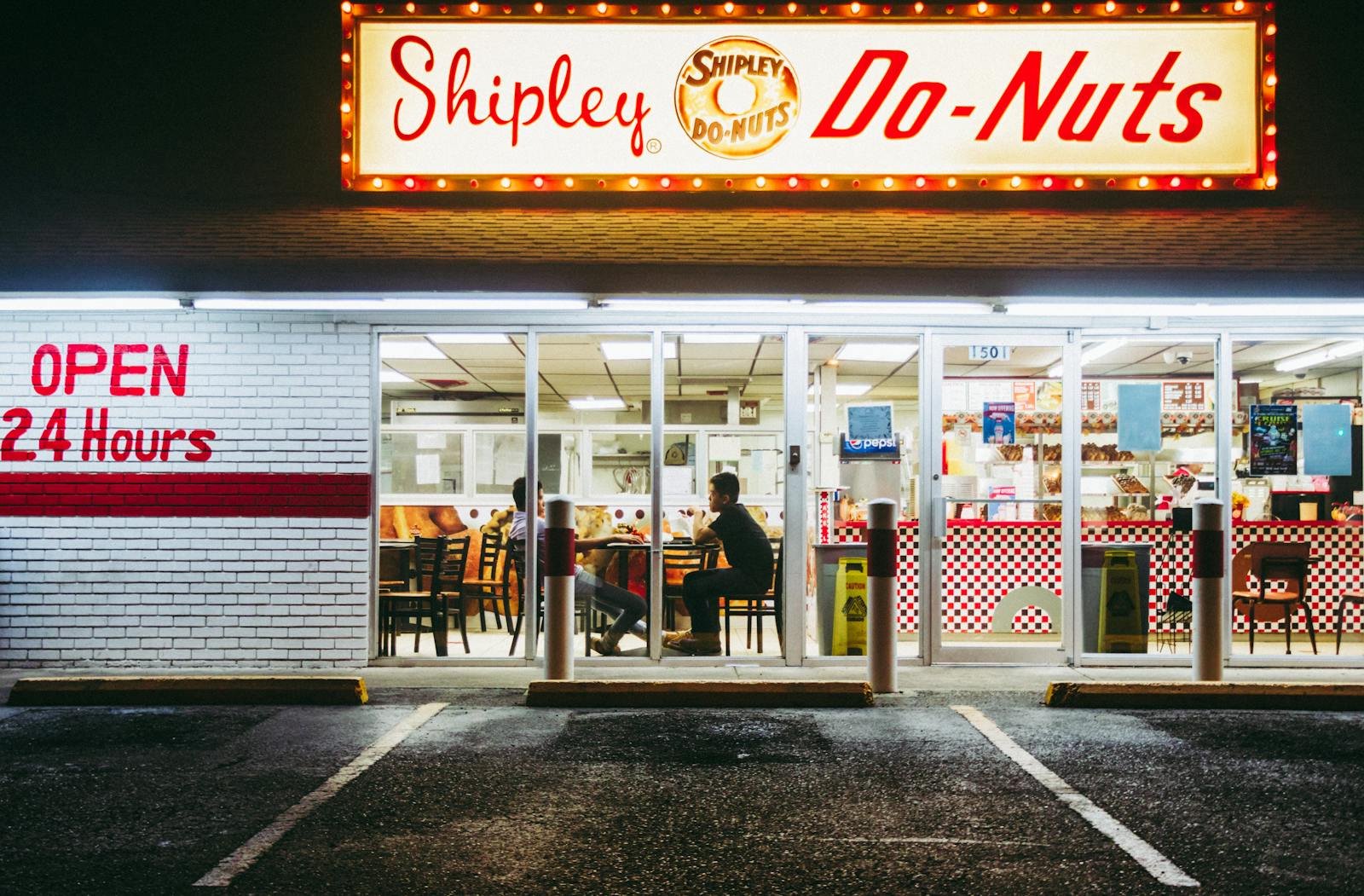 Brightly lit Shipley Do-Nuts shop in McAllen, TX, open 24/7. Nighttime urban scene.