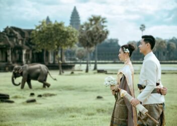 Elegant Cambodian couple in traditional attire at Angkor Wat with an elephant in the background.