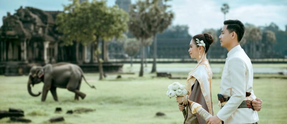 Elegant Cambodian couple in traditional attire at Angkor Wat with an elephant in the background.