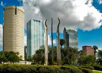 Tampa's skyline features tall skyscrapers and modern sculptures under a bright sky.