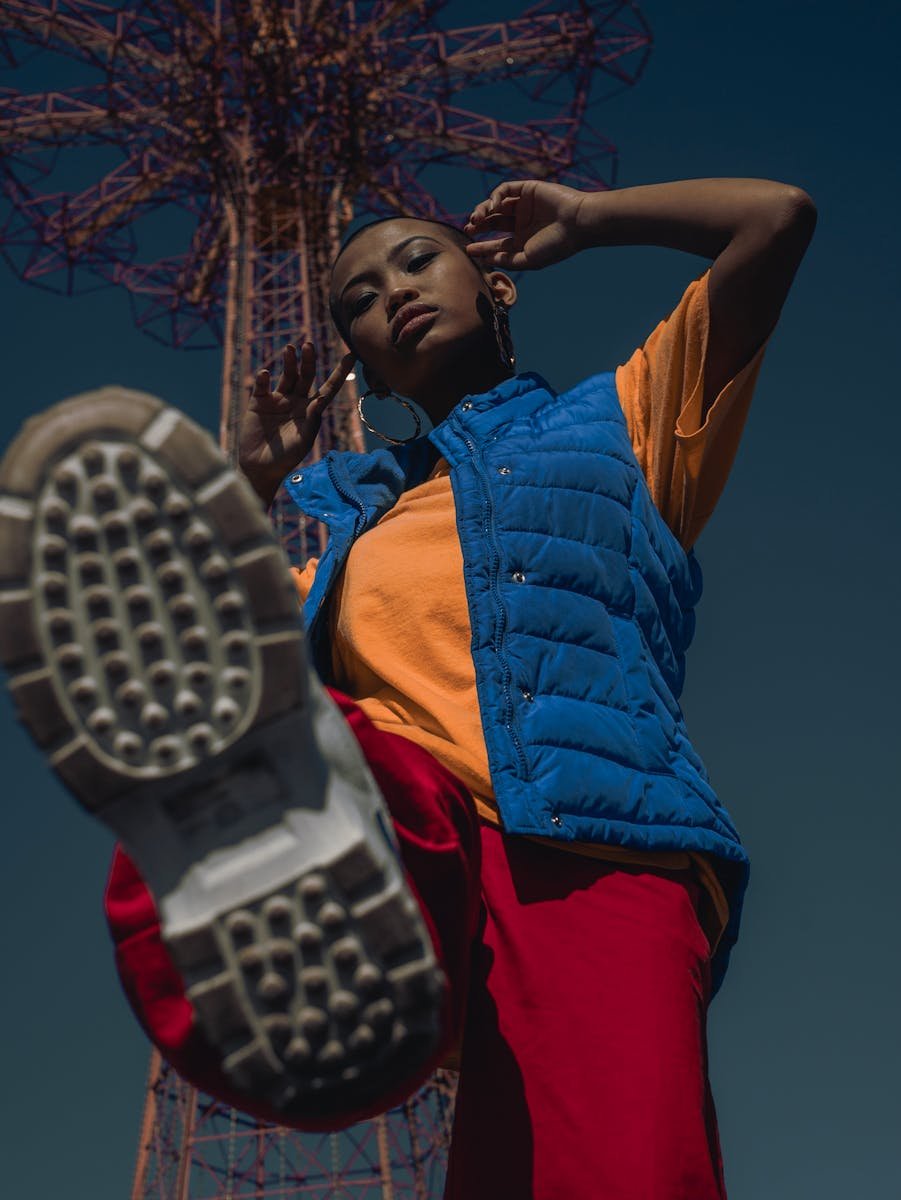 Stylish woman posing with iconic structure at Coney Island, NY in vibrant attire.