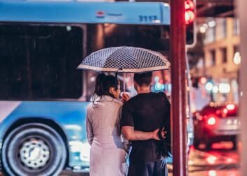 A couple stands under an umbrella, embracing on a rainy urban street at night.