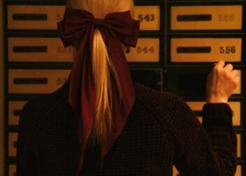 Back view of a woman wearing a burgundy bow facing numbered lockers in moody lighting.