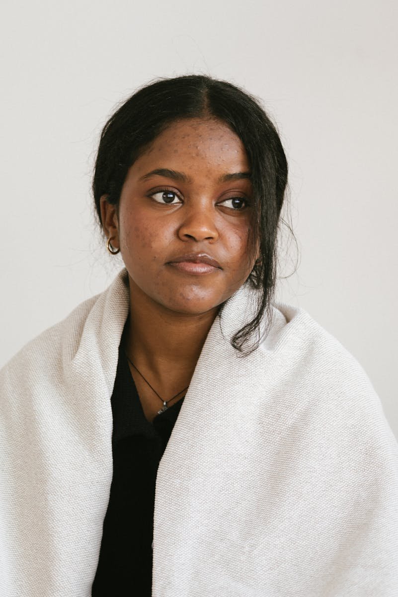 A contemplative young woman in a studio setting, wrapped in a light blanket.