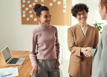 Business colleagues in an office shaking hands and smiling, showcasing teamwork and collaboration.