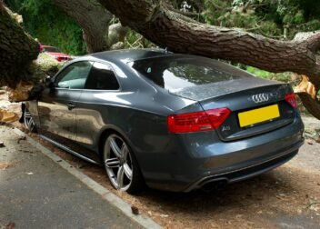 A broken Audi car crushed by a fallen tree in a UK street accident.