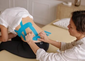 A professional therapist applies kinesiology tape to a woman's back during a physiotherapy session.