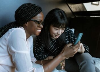 Two women relaxed on a sofa, sharing and enjoying moments on a smartphone.