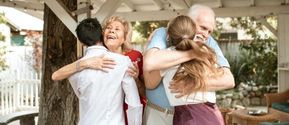 A joyful family reunion outdoors with warm hugs and smiles under a wooden pergola.