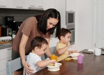 A mother helps her toddlers enjoy breakfast in a modern kitchen setting.