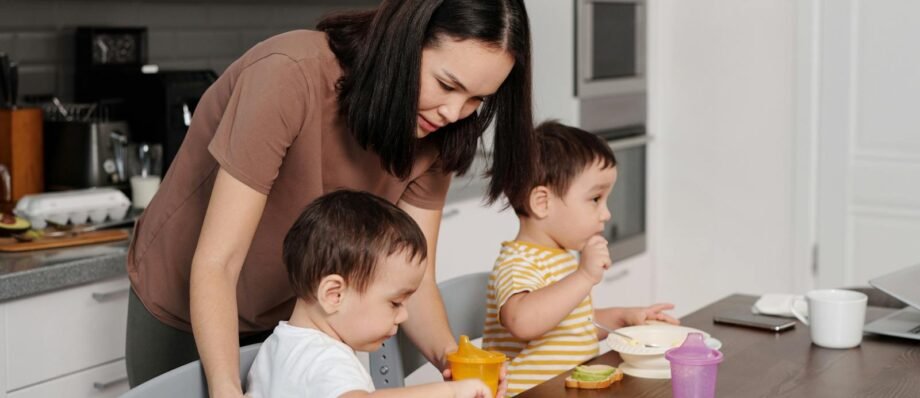 A mother helps her toddlers enjoy breakfast in a modern kitchen setting.