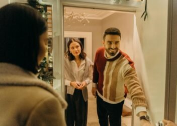 A couple greeting a guest at their doorway, capturing the warmth of a home during the holiday season.