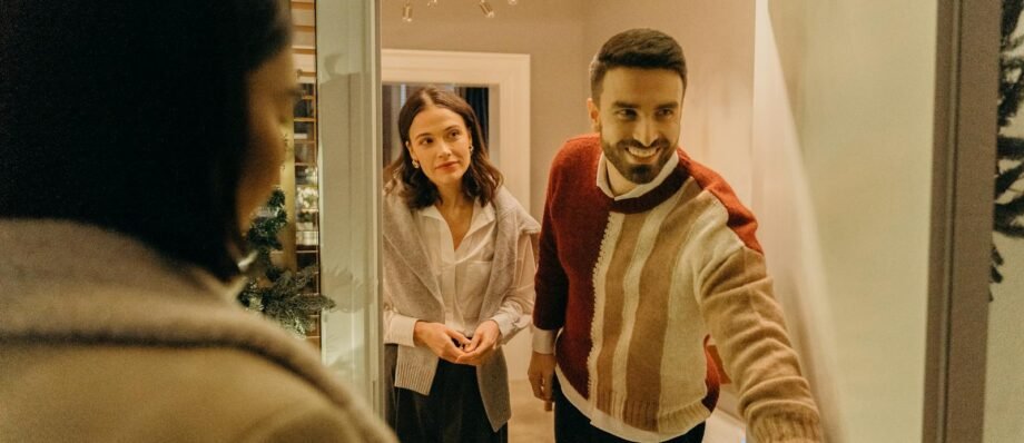 A couple greeting a guest at their doorway, capturing the warmth of a home during the holiday season.