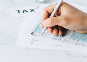 Hand completing tax forms with a pen, symbolizing financial deadline and time urgency.