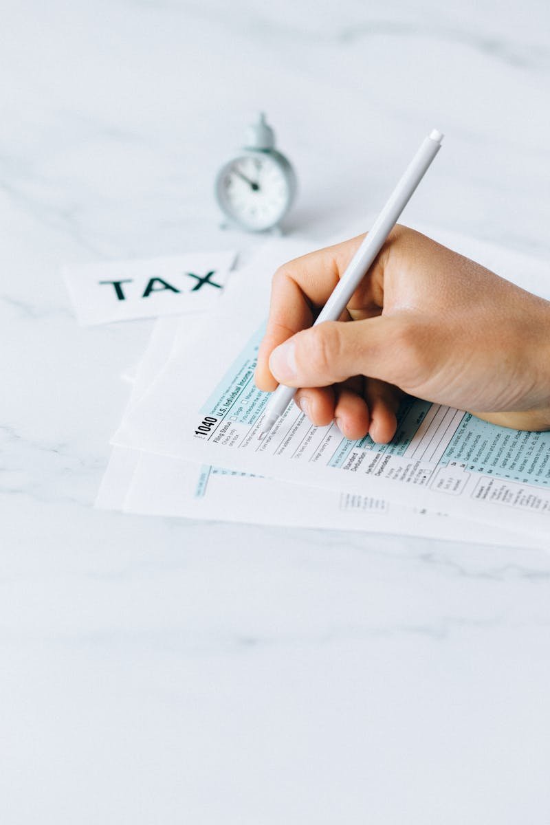 Hand completing tax forms with a pen, symbolizing financial deadline and time urgency.