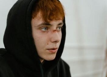 Teenager in a black hoodie looks away, revealing a fresh facial wound.