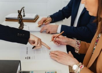 Hands signing a divorce decree, with a justice statue nearby, symbolizing legal proceedings.