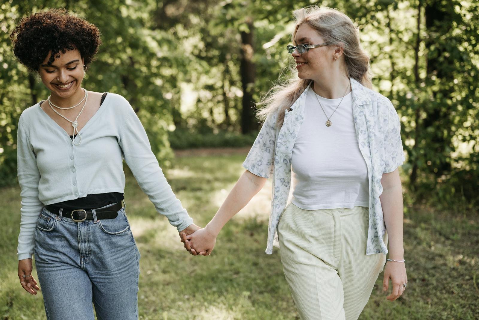 A loving couple holds hands while strolling through a lush, sunny park setting.