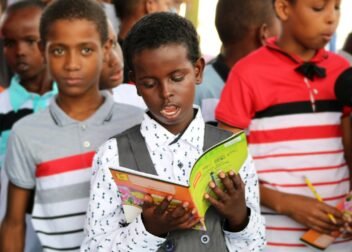 man in red and white polo shirt holding yellow book