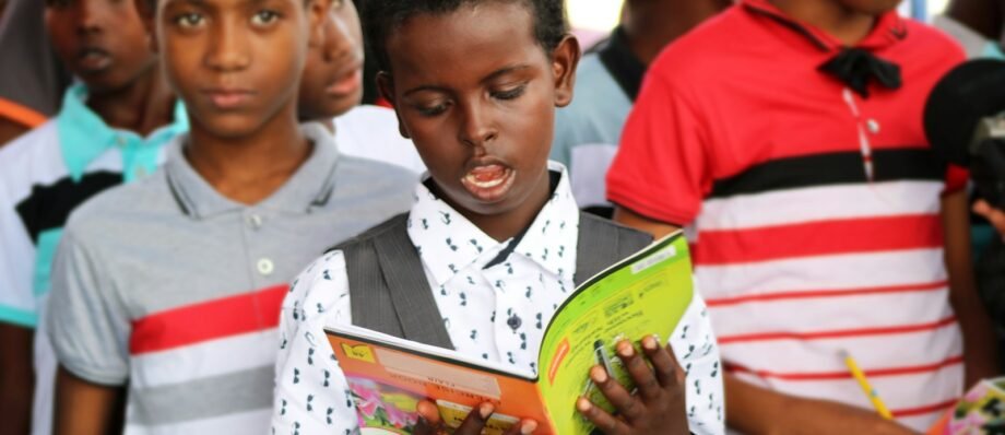 man in red and white polo shirt holding yellow book